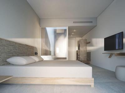 Modern hotel room with double bed, wall-mounted TV, and large glass shower in the background.