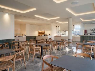 Sala colazione luminosa e moderna con sedie e tavoli in legno in un hotel.