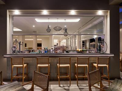 Area bar di hotel moderna con sgabelli in legno e bancone illuminato sotto vetro protettivo.