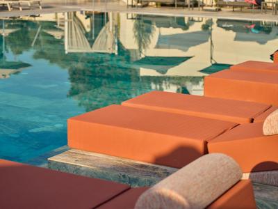 Area piscina con lettini arancioni e acqua azzurra cristallina in un resort.
