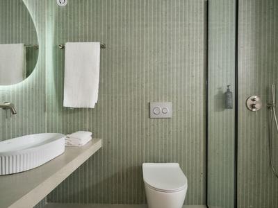 Bagno moderno con piastrelle verdi, lavabo bianco e WC accanto a una doccia in vetro.