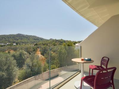 Balcone dell'hotel con tavolo, sedia e vista panoramica sulle colline verdi e cielo azzurro.