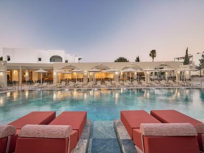 Hotel con grande piscina circondata da lettini rossi e architettura moderna al crepuscolo.