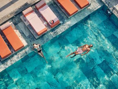 Piscina con acqua azzurra limpida, lettini arancioni e due persone che si rilassano.