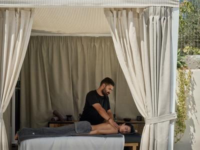 Uomo che massaggia una persona su un lettino da massaggio in un'area privata circondata da tende.