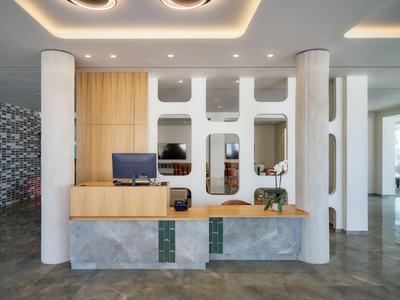 Reception di hotel moderna con legno chiaro, marmo grigio e colonne decorative.