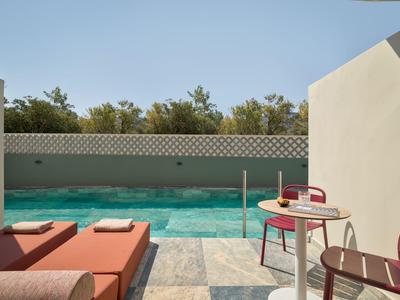 Area esterna moderna con piscina, lettini e sedute circondate da muri bianchi e alberi.
