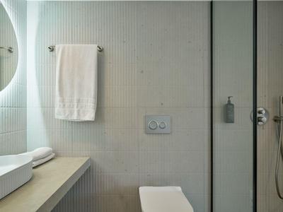 Bagno moderno con lavabo, asciugamano bianco e cabina doccia in una camera d'hotel.