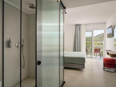 Camera d'albergo moderna con doccia, letto matrimoniale e balcone con vista sulle montagne.