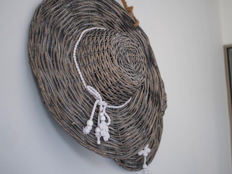 Large round woven sunhat made of gray material with white ties hanging on the wall.