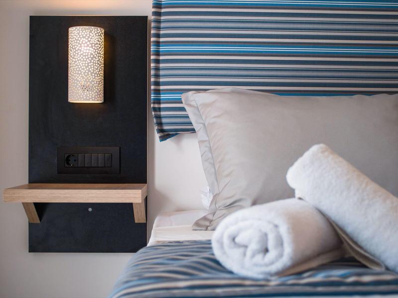 A hotel bed with light gray pillows, two rolled white towels, and a blue headboard.