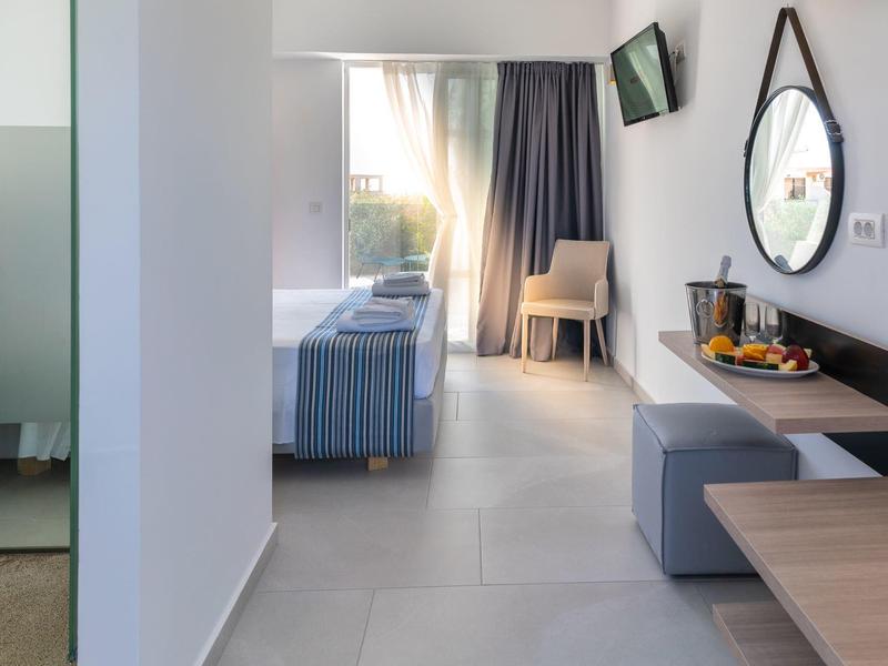 Bright hotel room with bed, chair, mirror, and drinks on the sideboard.