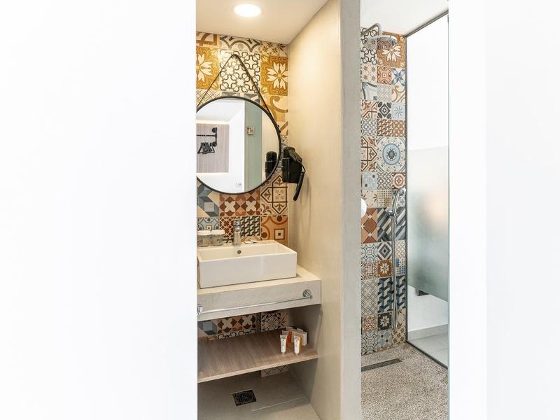 Modern bathroom area with sink, round mirror, and colorful tiles on the wall.