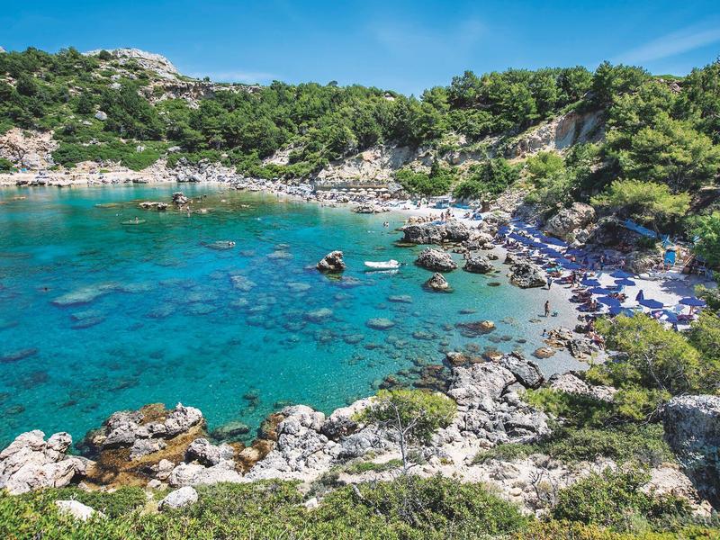 Clear turquoise water in a rocky cove with green vegetation and blue sky.