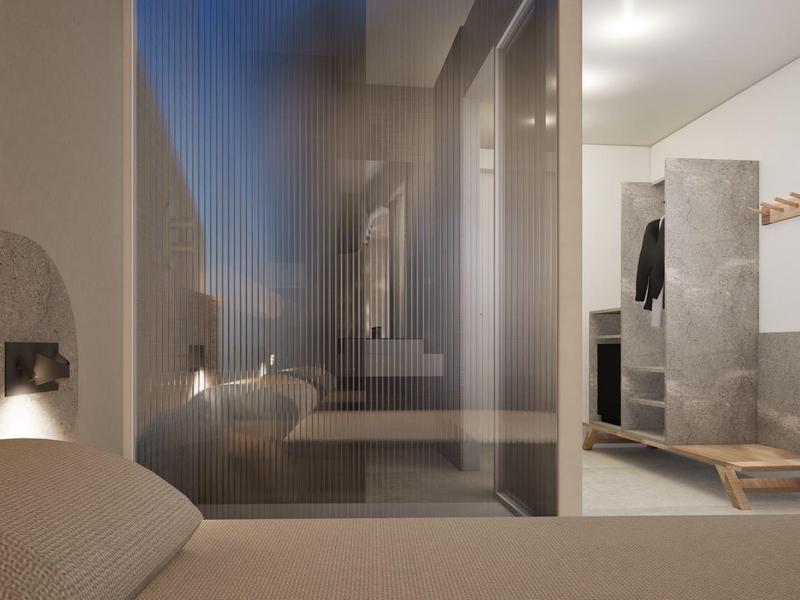 Modern hotel room with light walls, beige bed, and open bathroom with glass partition.