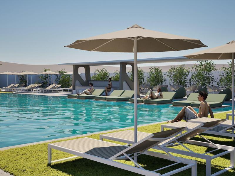 Relaxed person sitting on lounge chair by pool with umbrellas and other lounge chairs.