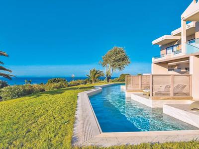 Modern pool with glass fence and sea view next to a house under clear sky.