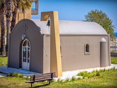 Piccola cappella affascinante con pareti grigio chiaro e porta ad arco, circondata da palme.