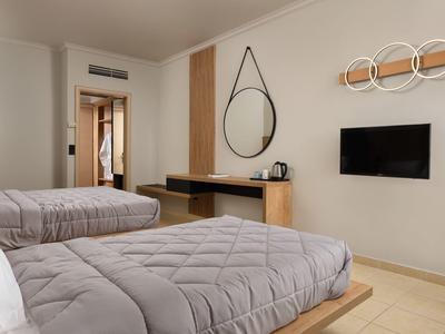 Camera d'hotel moderna con due letti, TV a schermo piatto e specchio rotondo sulla parete.