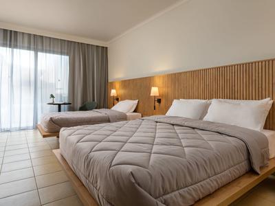 Camera d'hotel luminosa con due letti e una grande finestra con tende.