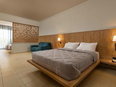 Camera d'hotel moderna con letto grande, poltrone e luce naturale attraverso grandi finestre.
