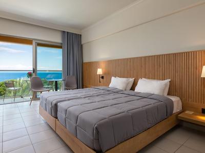 Modern hotel room with double bed and sea view through large windows.