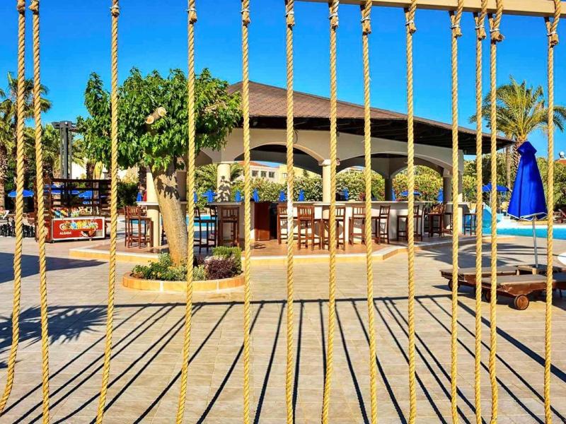 Vista attraverso una ringhiera dorata su un'area piscina soleggiata con lettini e palme.