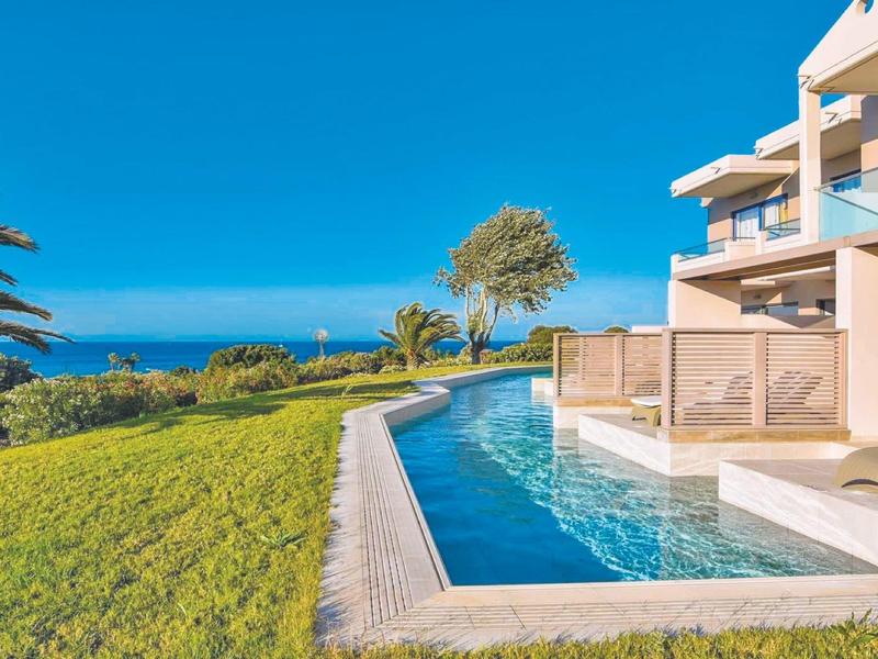 Resort moderno con piscina privata, prato adiacente e vista mare sotto un cielo sereno.