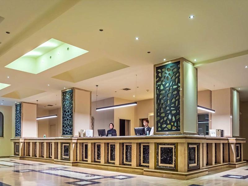 Ampia reception dell'hotel con pannellature in legno elegante e illuminazione calda.