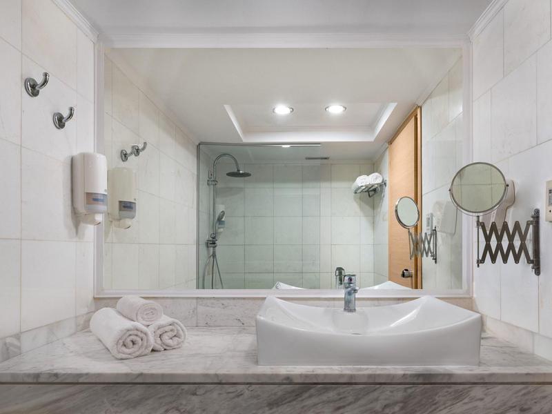 Bagno moderno con lavabo, grande specchio e doccia piastrellata sullo sfondo.