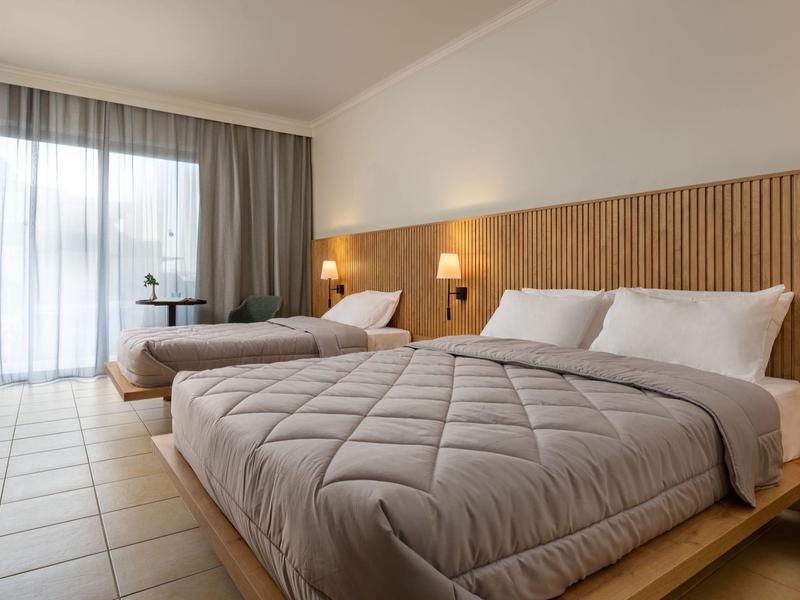 Camera d'hotel luminosa con due letti e una grande finestra con tende.