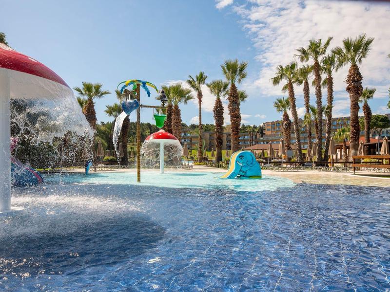 Piscina per bambini con funghi d'acqua e palme in una soleggiata località turistica