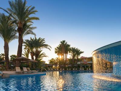 Pool with waterfall and palm trees at sunset in a resort.