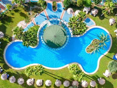 Aerial view of a tropical hotel pool with palm trees, sun loungers, and umbrellas