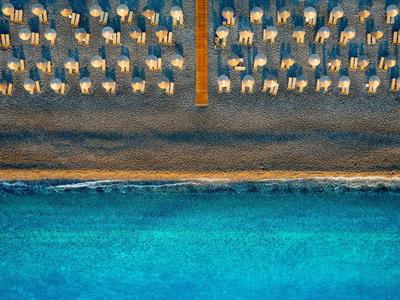 Letecký pohled na písečnou pláž s řadami slunečníků a lehátek vedle čistého modrého moře.