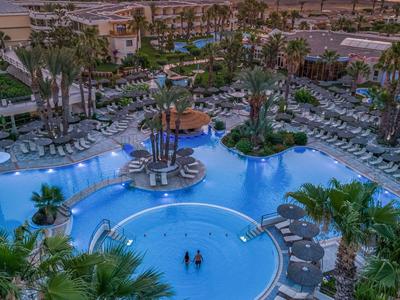 Large hotel pool with sun loungers and palm trees at sunset.