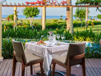 Elegant set table with white cloths and glasses, with garden and sea view in the background.