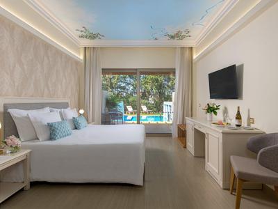 Moderní hotelový pokoj s manželskou postelí, TV, pohodlným křeslem a velkým oknem s výhledem na bazén.