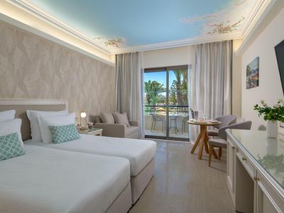 Modern hotel room with two single beds, balcony, and view of palm trees.