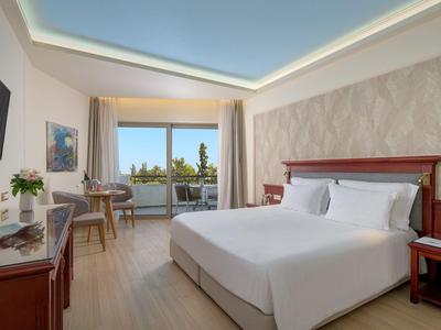 Světý hotelový pokoj s velkou postelí, TV, pracovním stolem a balkonem s posezením a výhledem.