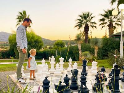 A man and a child stand on an oversized outdoor chessboard at sunset.
