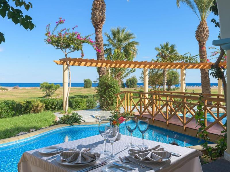 Venkovní jídelní stůl pro čtyři u bazénu s palmami a výhledem na oceán