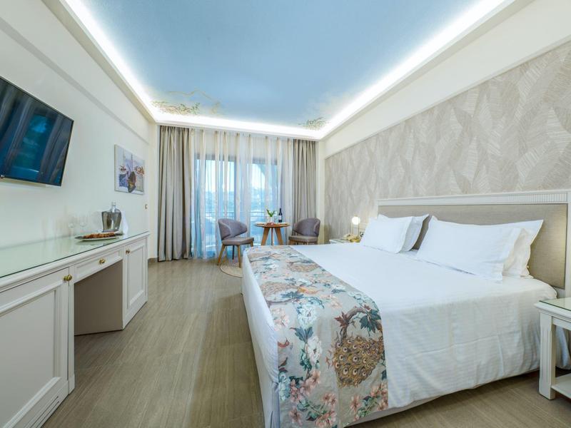 Moderní hotelový pokoj s postelí king-size, televizí s plochou obrazovkou a posezením u okna.