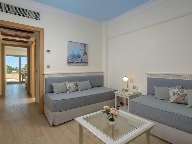 Moderní hotelový pokoj s dvěma pohovkami, konferenčním stolkem a výhledem na balkon.