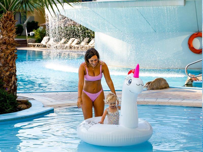 Žena a dítě v růžových plavkách si užívají slunečný bazén na bílém nafukovacím jednorožci