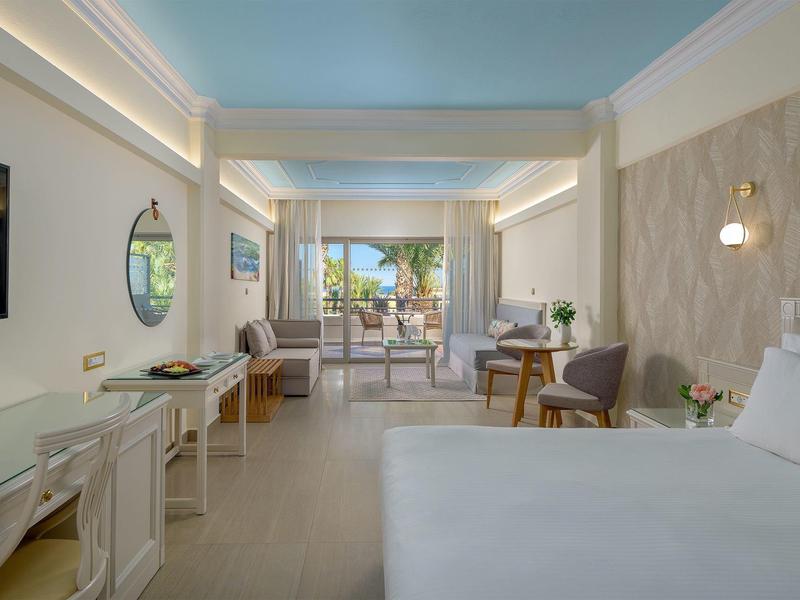 Prostorný hotelový pokoj s velkou postelí, psacím stolem, posezením a balkonem s výhledem na oceán.