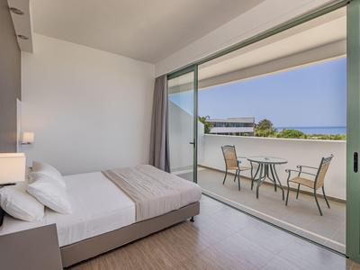 Camera d'hotel moderna con letto e balcone con vista mare, tavolo e sedie all'esterno.