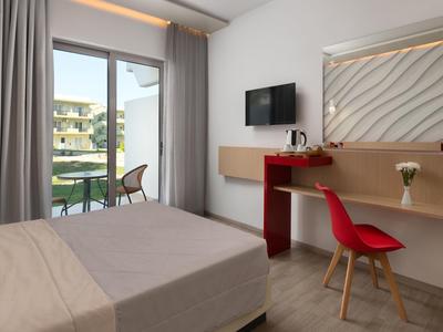 Camera d'hotel moderna con letto, sedia rossa, scrivania, TV e balcone con posti a sedere esterni.