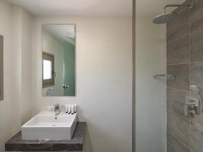 Bagno moderno con lavabo, specchio, finestra e doccia con piastrelle grigie.