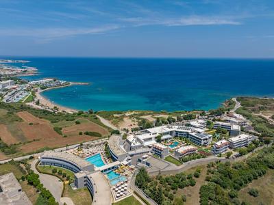 Un resort costiero con vari edifici, piscine e campi verdi vicino al mare blu.